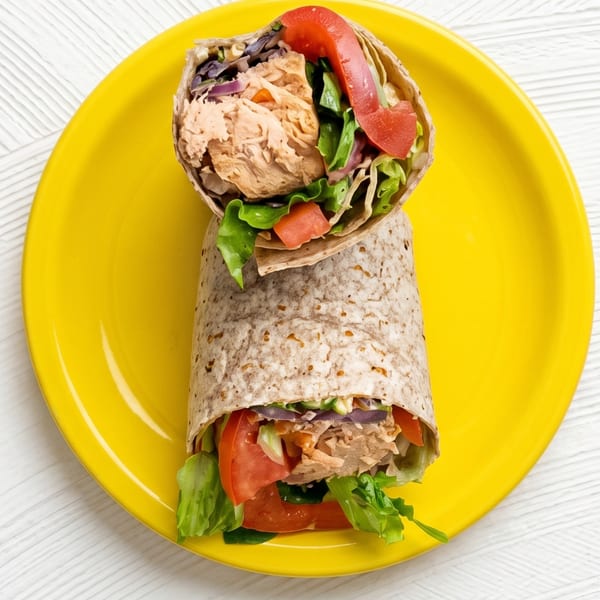 Two chicken wraps with lettuce, tomato, and red onion on a bright yellow plate.