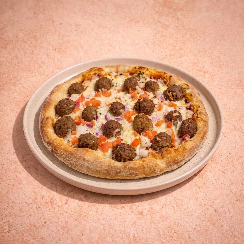 Round pizza topped with meatballs, melted cheese, diced tomatoes, and onions on a ceramic plate.