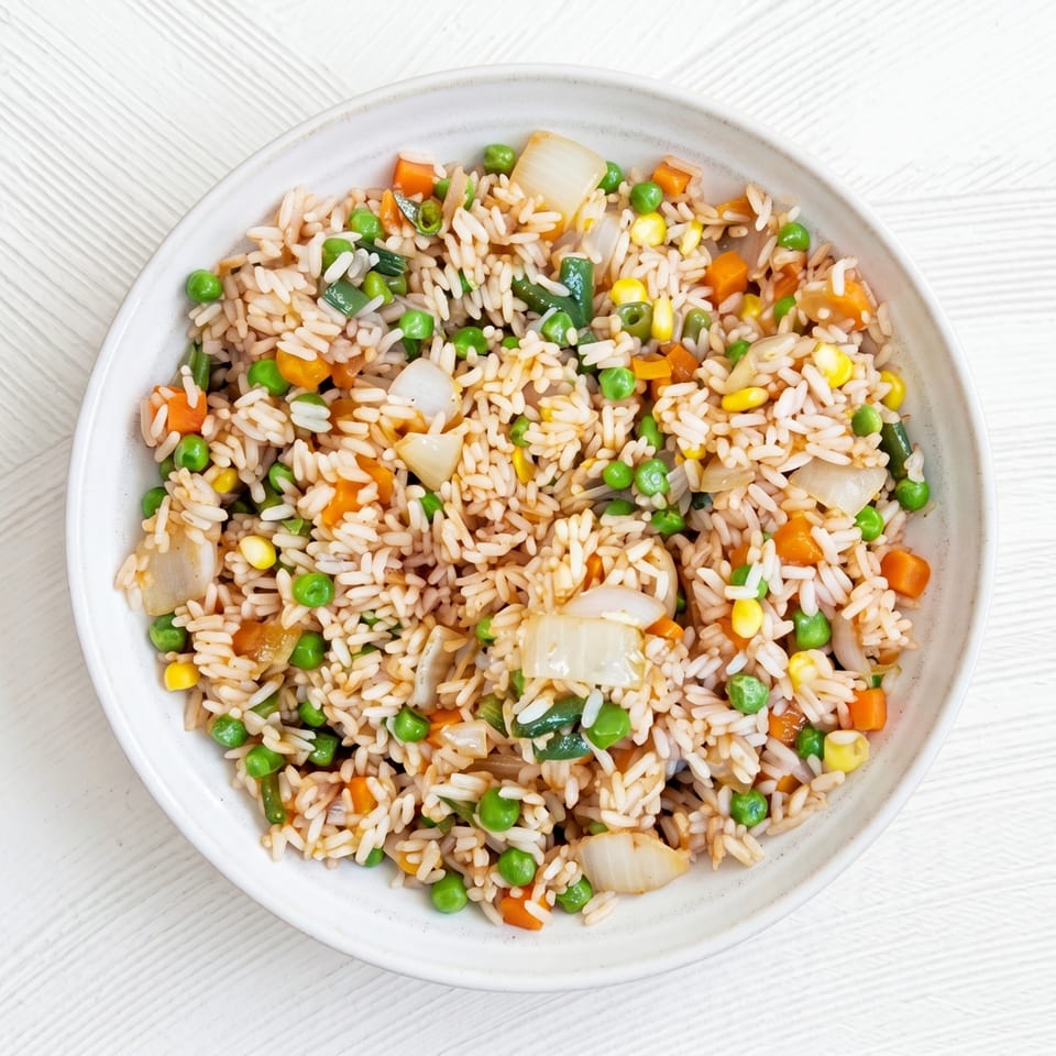 Overhead view of a white bowl filled with vegetable fried rice on a white textured surface.