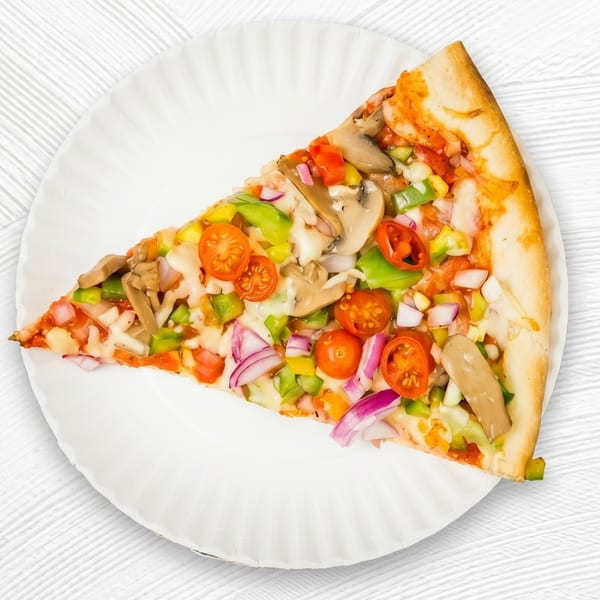 A colorful slice of vegetarian pizza with mushrooms, bell peppers, onions, and cherry tomatoes on a white paper plate.