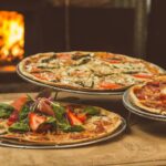 Trio of gourmet kosher pizzas in brooklyn with unique toppings near a wood-fired oven, ideal for food enthusiasts.
