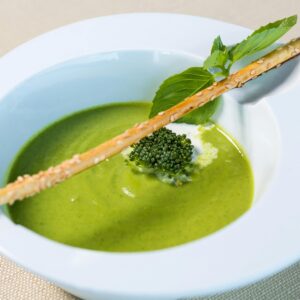 A bright green pea soup in a white bowl, garnished with croutons and herbs, elegantly presented.