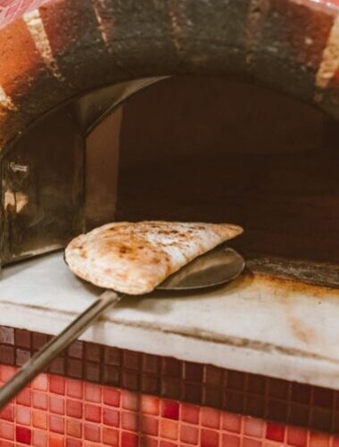 A calzone being taken out of a traditional Italian brick oven, showcasing rustic baking style.