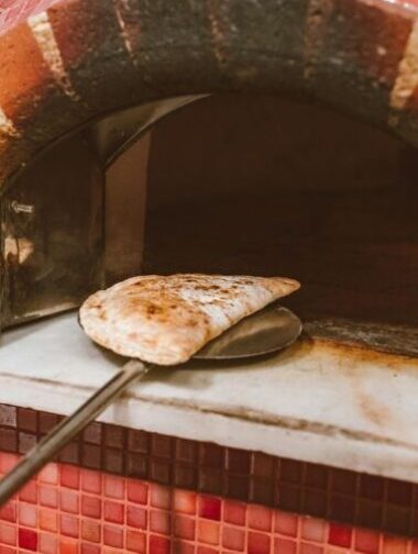 pexels-photo-5903396-5903396 A calzone being taken out of a traditional Italian brick oven, showcasing rustic baking style.